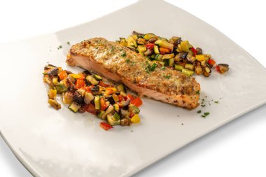 Otla pişirilmiş çıtır somon filetosu yanında da beyaz tabakta ratatouille.