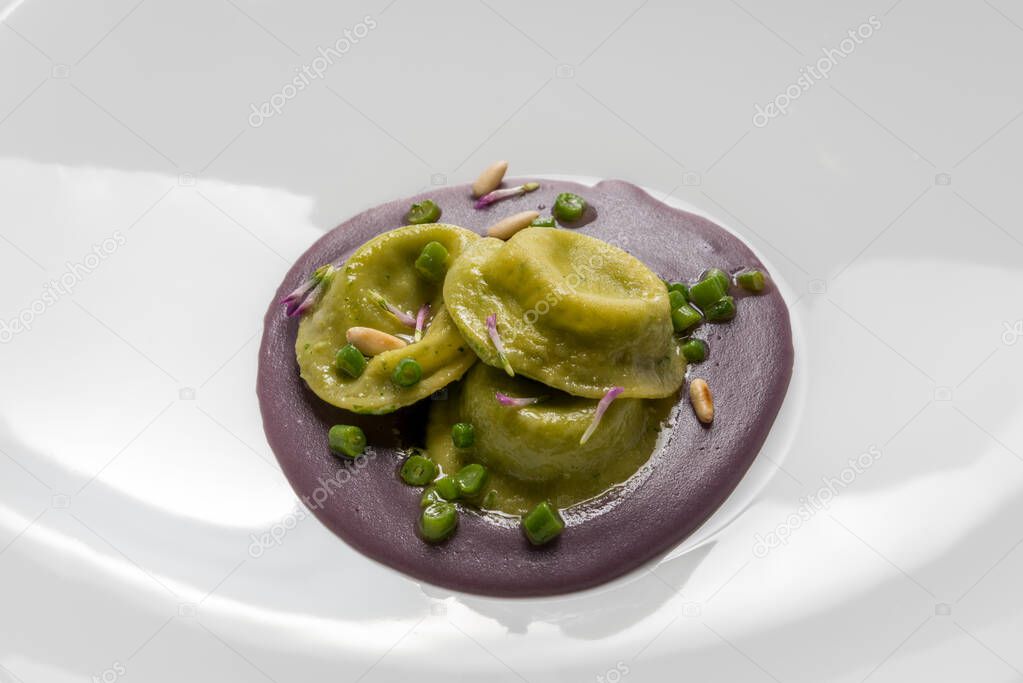 Green spinach tortelloni filled with cheese and vegetables, on beetroot puree with peas and pine nuts, close up