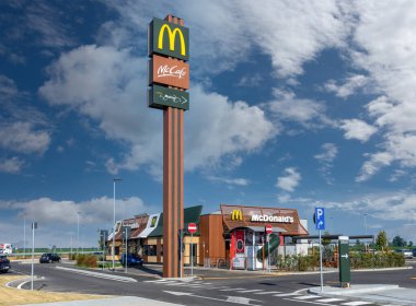 Savigliano, İtalya - 16 Haziran 2022: McDonalds 'ın yeni restoranı, üzerinde McCaf logosu ve beyaz bulutlu mavi gökyüzünde McDrive yazılı büyük totem işareti olan, McDonalds en büyük hamburger fast food zinciri.