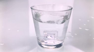 Buz küpleri, beyaz arka gronud 'un üzerine sıçramış saf su bardağına düşer.