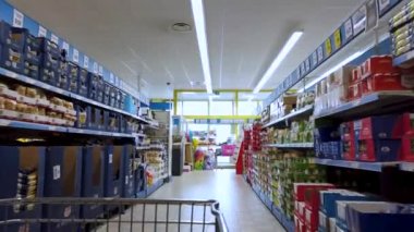 Fossano, Italy - July 21, 2022: subjective view of shopping cart that moves in aisle of shelves with pasta and canned food in italian Eurospin discount store supermarket.Tracking shot