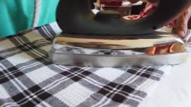 Woman hand with steam iron, close up while ironing and folding black and white checked cloth on ironing table
