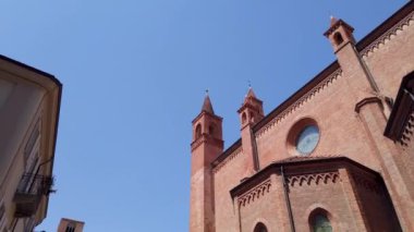 Tilt down from the cathedral spiers on Duomo square with the town hall among old houses and medieval towers  under beautiful sky in Alba, Langhe, Piedmont, Italy.