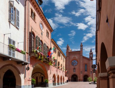 Alba, Langhe, Piedmont, Italy - August 16, 2022: the Town Hall with flowered balconies and medieval arcades in via Cavour, in the background Cathedral of San Lorenzo in Piazza Duomo