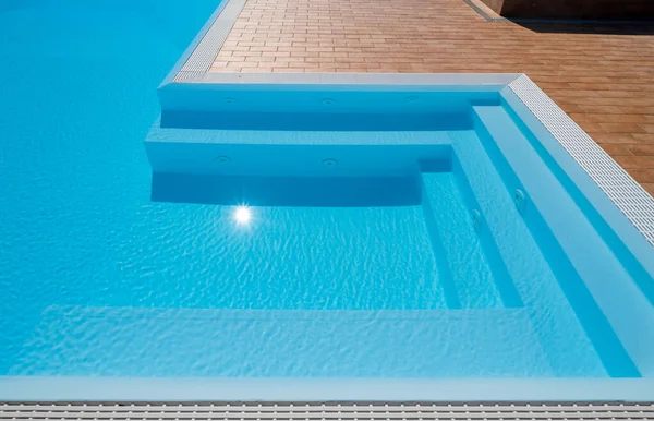 Swimming pool with steps in the jacuzzi corner with sun reflection
