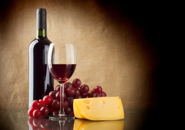 Bottle of red, a bunch of red grapes and a piece of cheese — Stock Photo, Image