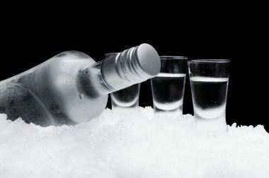 Bottle of vodka with glasses standing on ice on black background clipart