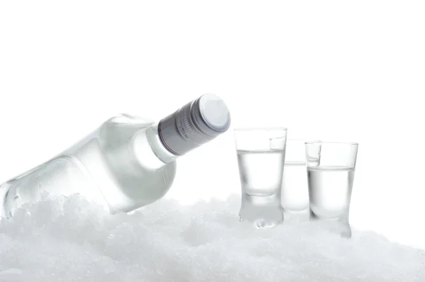 Botella y vasos de vodka acostado sobre hielo sobre blanco — Foto de Stock