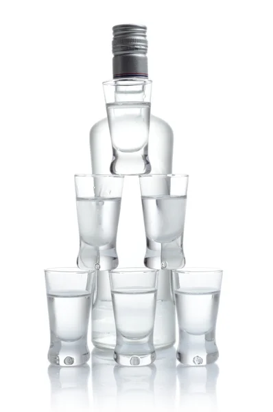 Garrafa com muitos copos de vodka isolados no fundo branco — Fotografia de Stock
