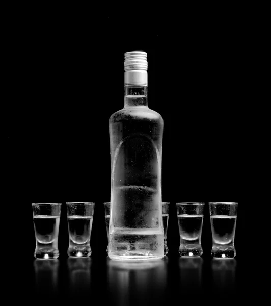 Botella y vasos de vodka de pie aislados sobre fondo negro — Foto de Stock