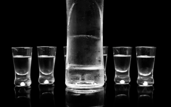 Garrafa e copos de vodka de pé isolados sobre fundo preto — Fotografia de Stock