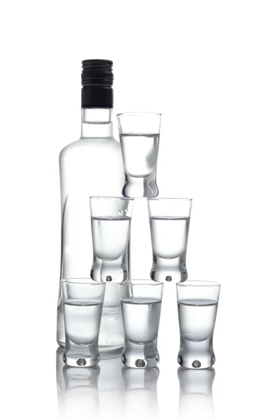 Garrafa com muitos copos de vodka isolados no fundo branco — Fotografia de Stock