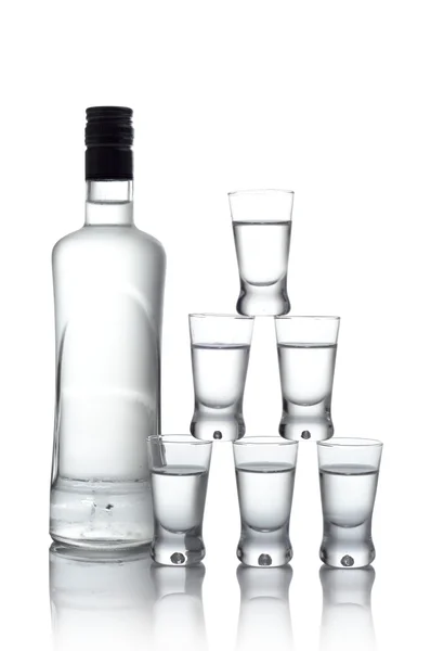 Garrafa com muitos copos de vodka isolados no fundo branco — Fotografia de Stock