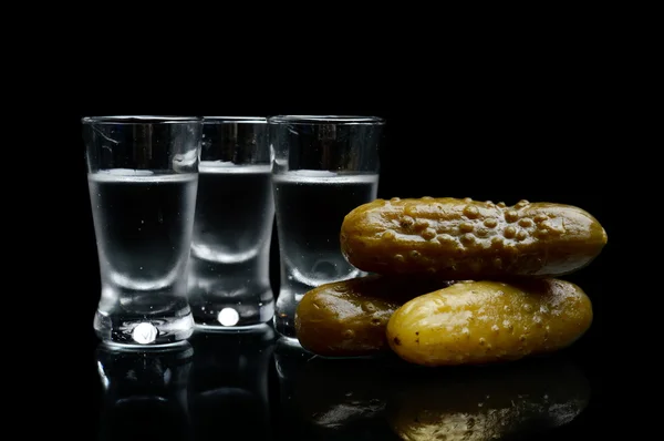 Muitos copos de vodka com pepinos em conserva isolados no fundo preto — Fotografia de Stock