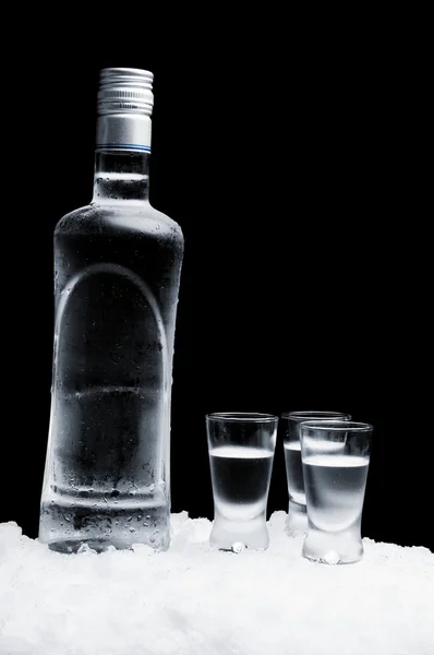 Пляшка горілки в окулярах, що стоять на льоду на чорному тлі — стокове фото