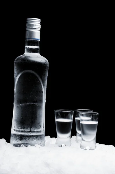 Flaska vodka med glasögon står på is på svart bakgrund — Stockfoto