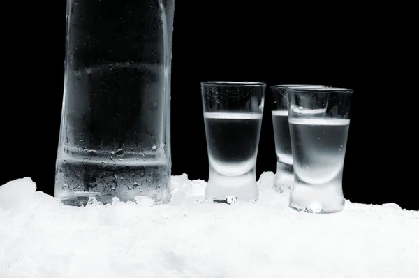 Fles wodka met glazen permanent op ijs op zwarte achtergrond — Stockfoto