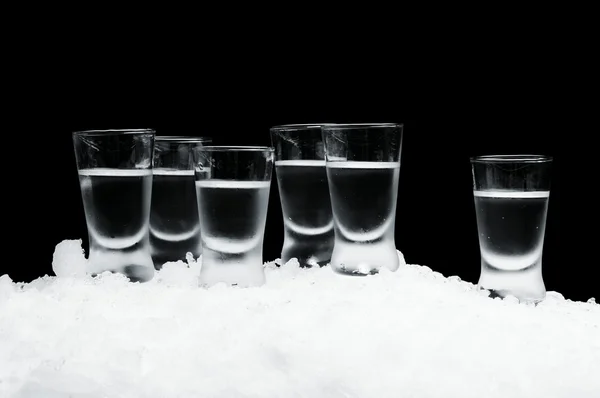 Many glasses of vodka standing on ice on black background — Stock Photo, Image