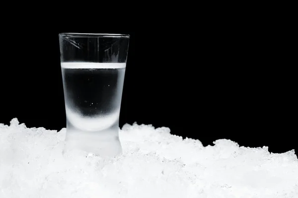 Glas vodka stående på is på svart bakgrund — Stockfoto