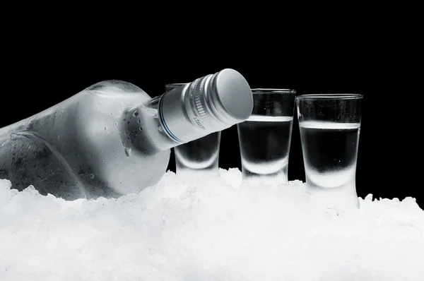 Bouteille de vodka avec des lunettes debout sur la glace sur fond noir — Photo