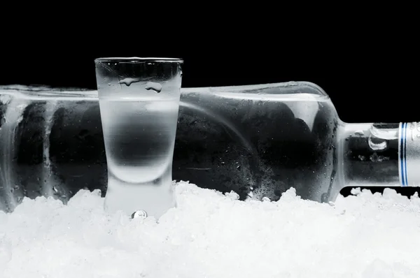 Bouteille avec verre de vodka couché sur glace sur fond noir — Photo