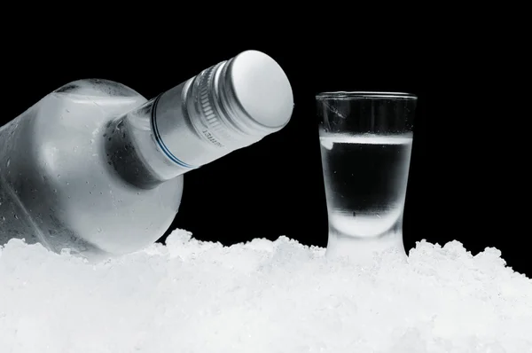 Bouteille avec verre de vodka couché sur glace sur fond noir — Photo