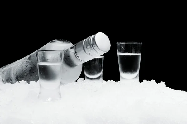 Flasche mit Wodkagläsern auf Eis liegend auf schwarzem Hintergrund — Stockfoto