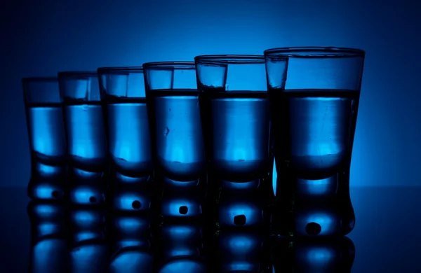 Muitos copos de vodka iluminados com luz de fundo azul — Fotografia de Stock