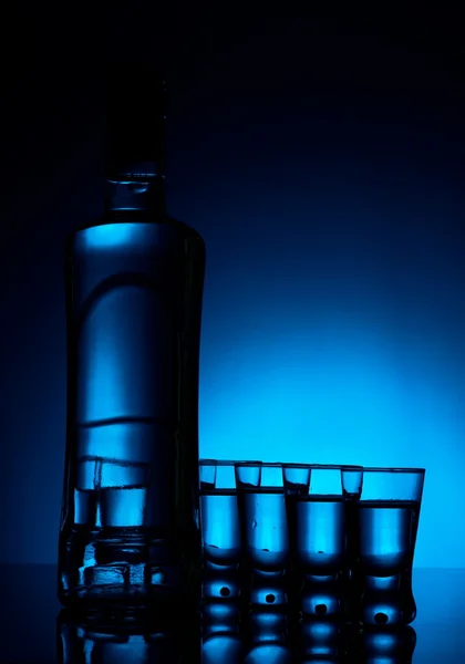 Bottiglia di vodka con molti bicchieri illuminati con retroilluminazione blu — Foto Stock