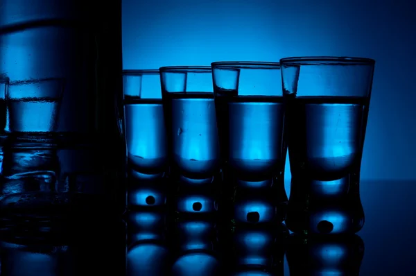 Bottiglia di vodka con molti bicchieri illuminati con retroilluminazione blu — Foto Stock