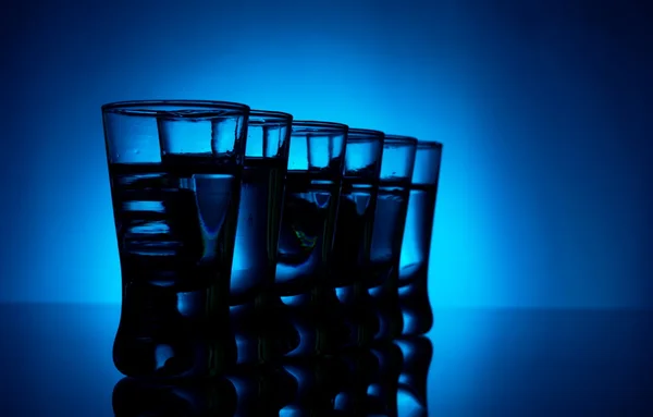 Många glas vodka lit med blå bakgrundsbelysning — Stockfoto