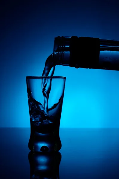 Vodka versata in un bicchiere illuminato con retroilluminazione blu Fotografia Stock