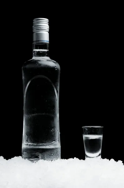 Garrafa com copo de vodka em pé no gelo sobre fundo preto — Fotografia de Stock