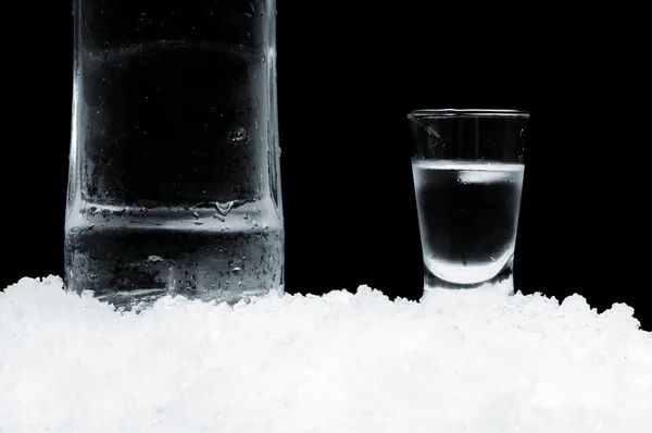 Garrafa com copo de vodka em pé no gelo sobre fundo preto — Fotografia de Stock