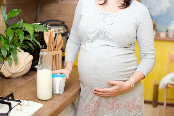 Donna incinta che beve latte in camera seduta su una sedia, Donna incinta felice che beve latte — Foto Stock