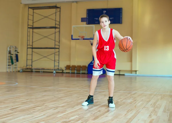 Basketball player with a ball in his hands and a red uniform. Basketball player practicing in the gym