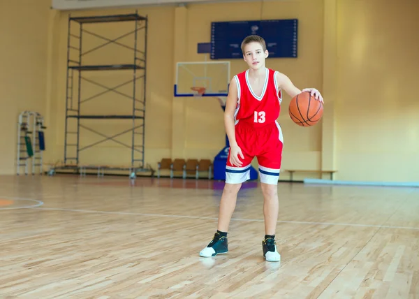 Basketball player with a ball in his hands and a red uniform. Basketball player practicing in the gym — Stock Photo, Image