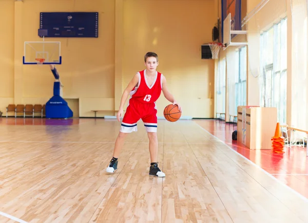 Jogador de basquetebol com uma bola nas mãos e um uniforme vermelho. Jogador de basquete praticando no ginásio — Fotografia de Stock