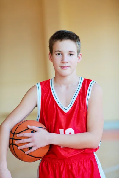 Basketball player with a ball in his hands and a red uniform. Basketball player practicing in the gym — Stock Photo, Image