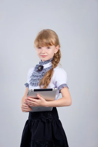 Маленькая школьница улыбается, используя цифровой планшет за столом — стоковое фото
