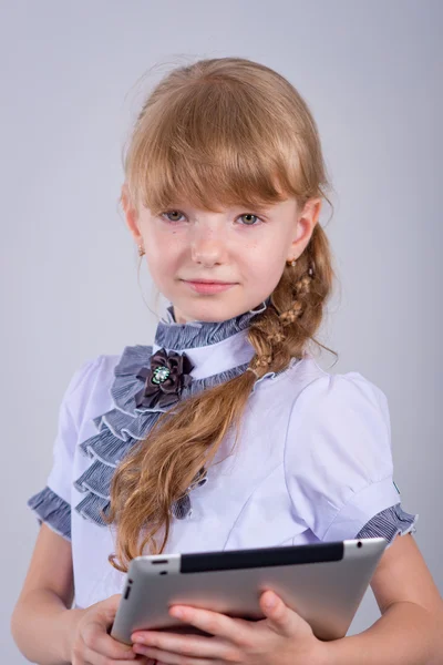 Pequeña colegiala sonriendo mientras usa la tableta digital en el escritorio — Foto de Stock