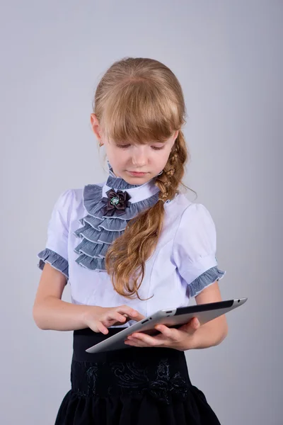 Kleine Schülerin lächelt, während sie digitales Tablet am Schreibtisch benutzt — Stockfoto