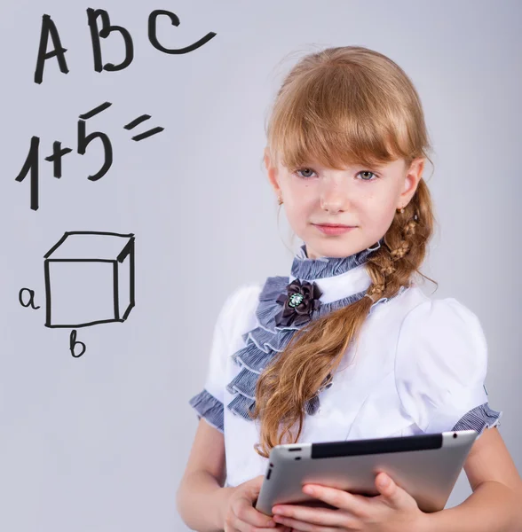 Kleine Schülerin lächelt, während sie digitales Tablet am Schreibtisch benutzt — Stockfoto