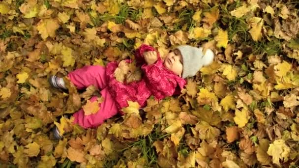 A small girl is lying on yellow leaves — Stock Video