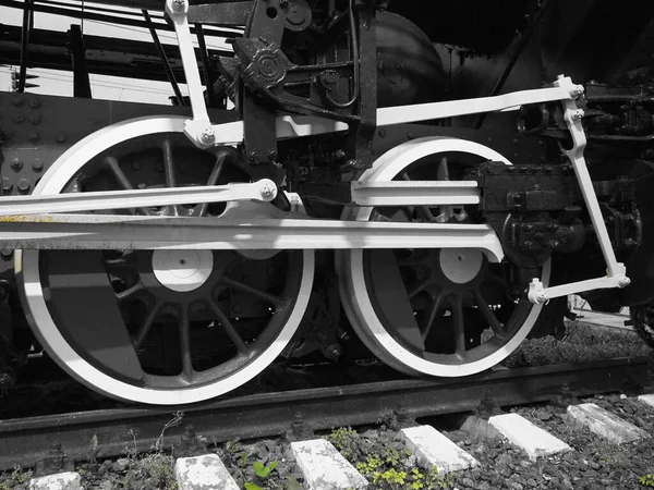 Treno retrò due ruote. Traverse e rotaie, meccanismi, pistoni e guide. Locomotiva dell'inizio del XIX secolo con motore a vapore. Ruote in bianco e nero con erba verde. Stile vintage — Foto Stock