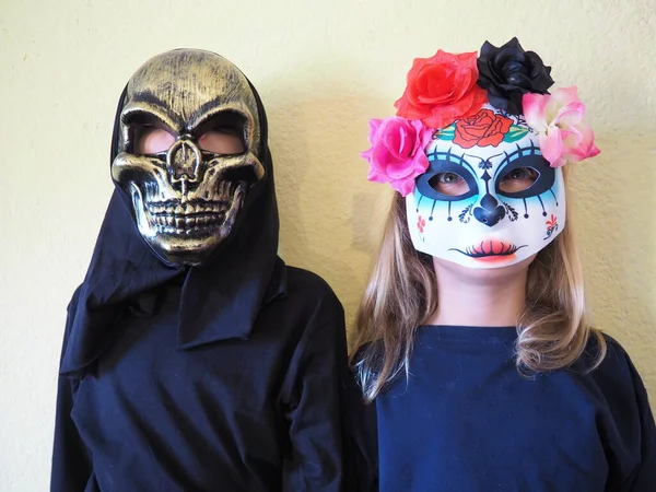 Barn klädda i svarta kostymer och läskiga halloween masker. Flicka i en mexikansk Kalaka Calavera mask. En pojke som bär en hemsk dödskallemask med svart huva. Alla helgons afton eller Alla helgons afton tema. — Stockfoto