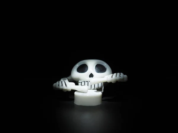 Calavera con muslos y tambor. Terrible juguete de relojería. El esqueleto está hecho de cráneo, huesos, manos y dedos. Fondo negro. Halloween y el tema de terror. Cráneo blanco con cuencas oculares negras —  Fotos de Stock