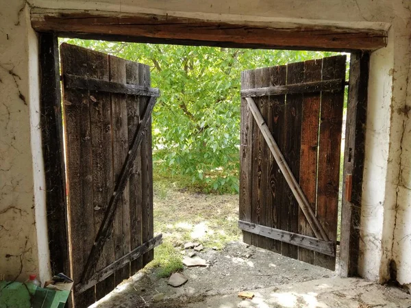Beautiful old wooden open door. Inside view of the room. Crib doors, stall for livestock or garage. Wooden beams and doorway. Summer greens from the door — Stock Photo, Image