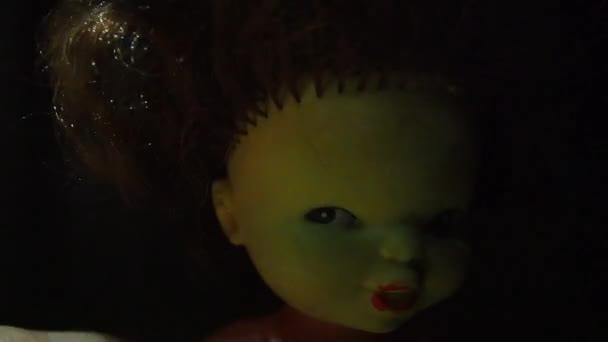 Egy ijesztő, sárga arcú vintage baba nézi a nézőt. Egy fénysugár lengi a fejet. Ravasz nézés, kusza sötét haj és titokzatos félmosoly. Éjszaka és sötétség. Horror Halloween koncepció — Stock videók