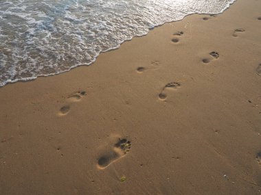 Tatil köyünün kumsalındaki suyun yakınındaki kumda insan ayağının izleri. Gün batımında kuvars kumu. Dalgadaki düşük güneş ışınlarının yansıması. Tatilde özgürlük, rahatlama ve zevk.